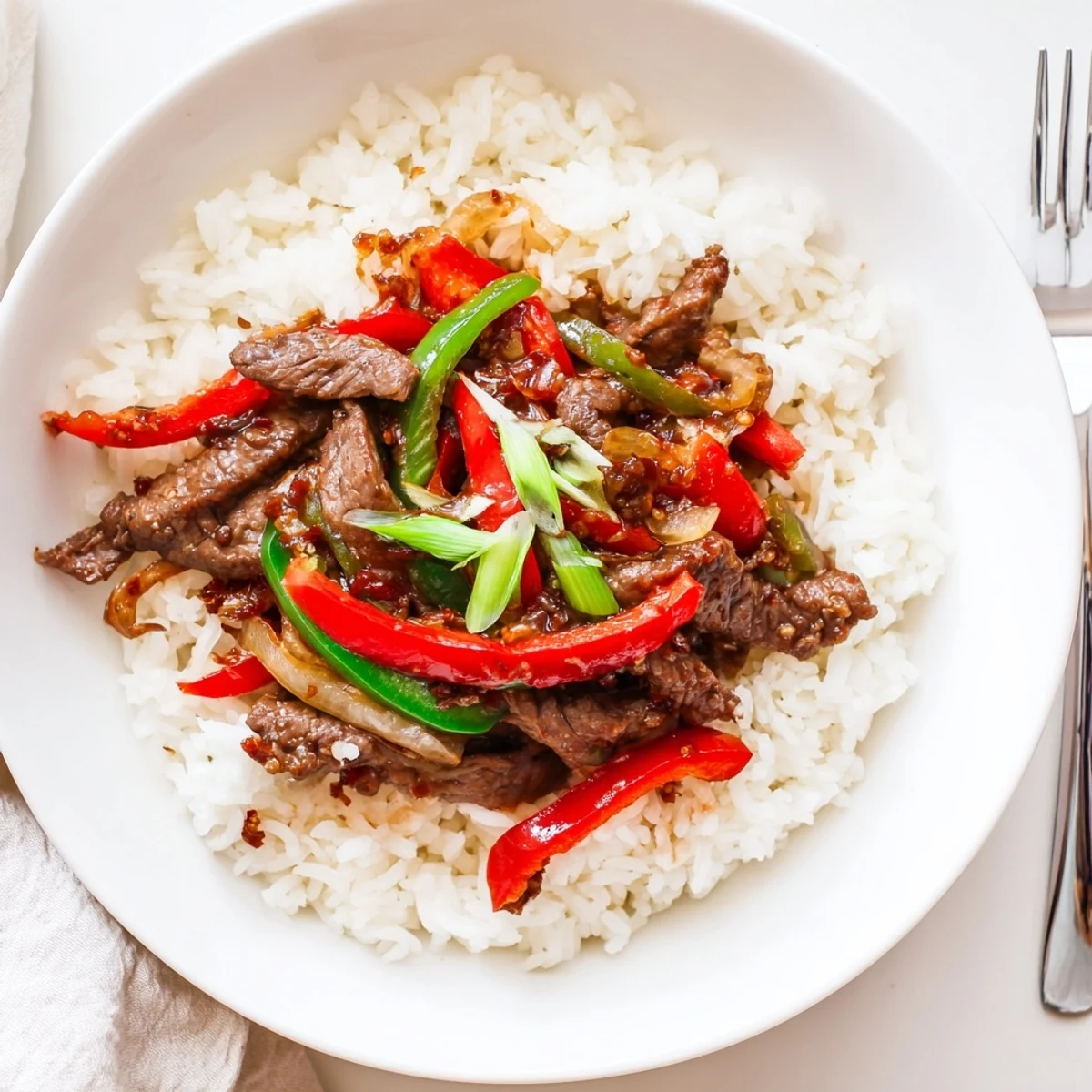 Fluffy jasmine rice topped with colorful bell peppers and tender beef coated in a spicy, glossy sauce for a vibrant stir-fry.