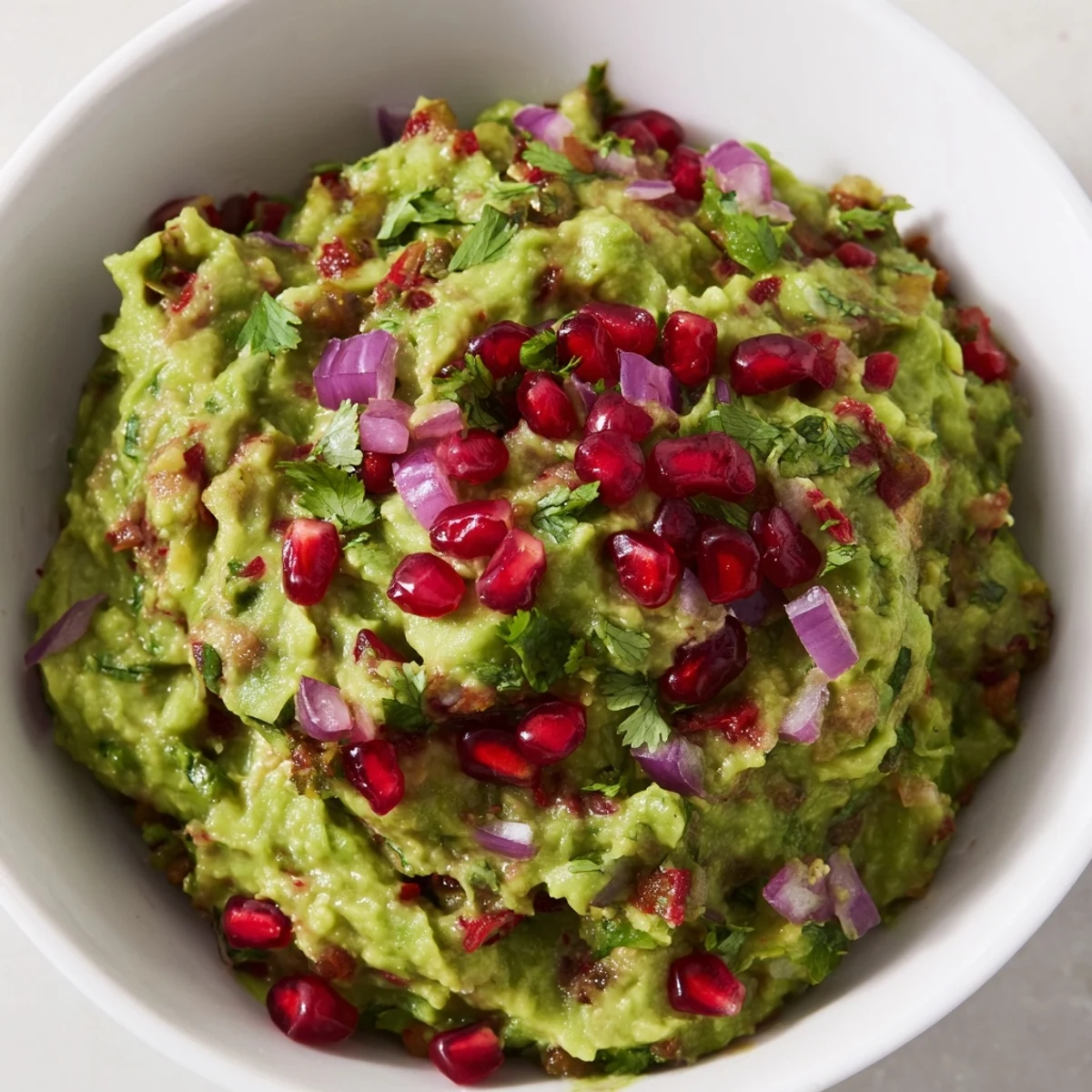 A vibrant bowl of Touchdown Spicy Guacamole, topped with pomegranate seeds, served with blue corn tortilla chips for a game day snack.