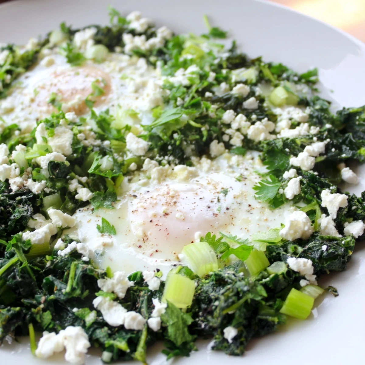 Overhead view of Green Shakshuka with spinach and feta, garnished with avocado slices and lemon wedges on a rustic kitchen table.