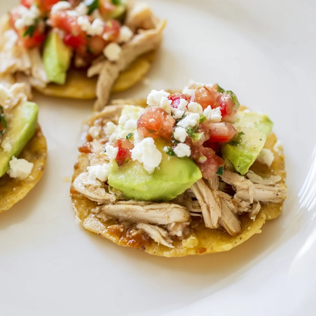 Golden-crisp mini chicken tostadas topped with fresh avocado and creamy sour cream on a platter.  