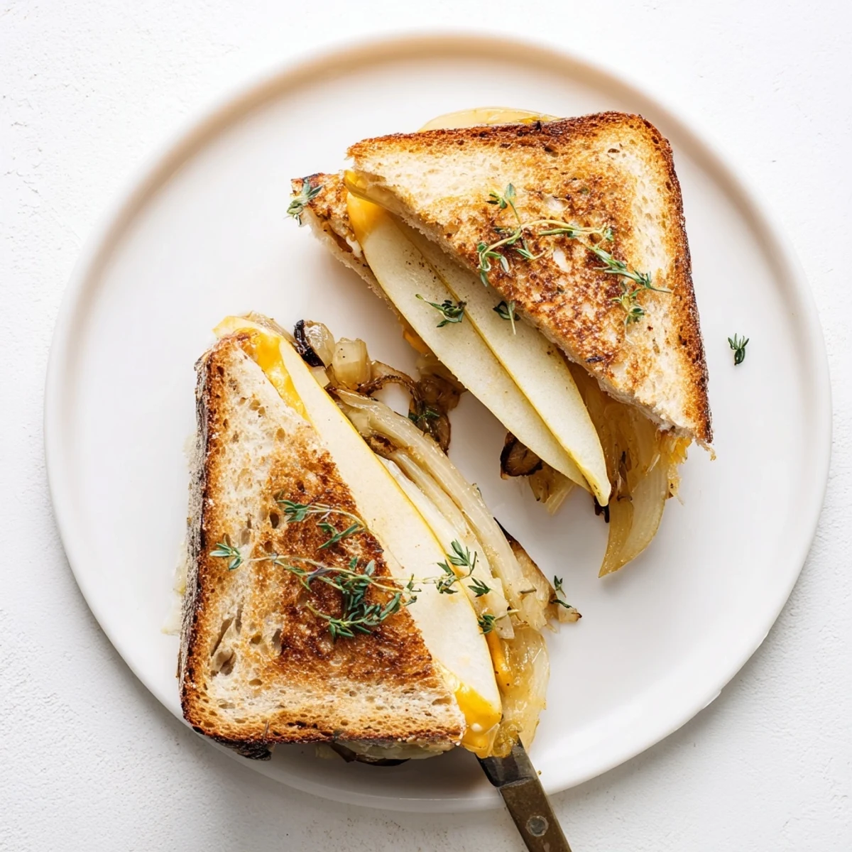 A close-up shows the gooey cheese pull from a warm Pear, Apple & Grilled Cheese with Caramelized Onions on a plate.