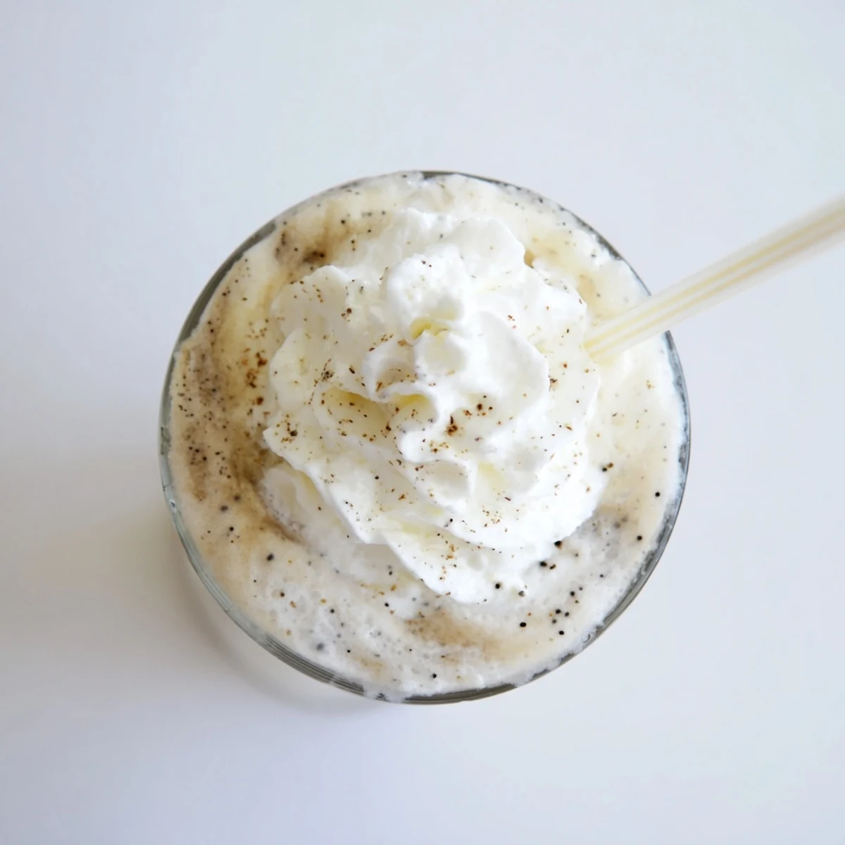 Two servings of creamy Vanilla Bean Frappuccino with swirls of whipped cream and ice cubes on a table.  