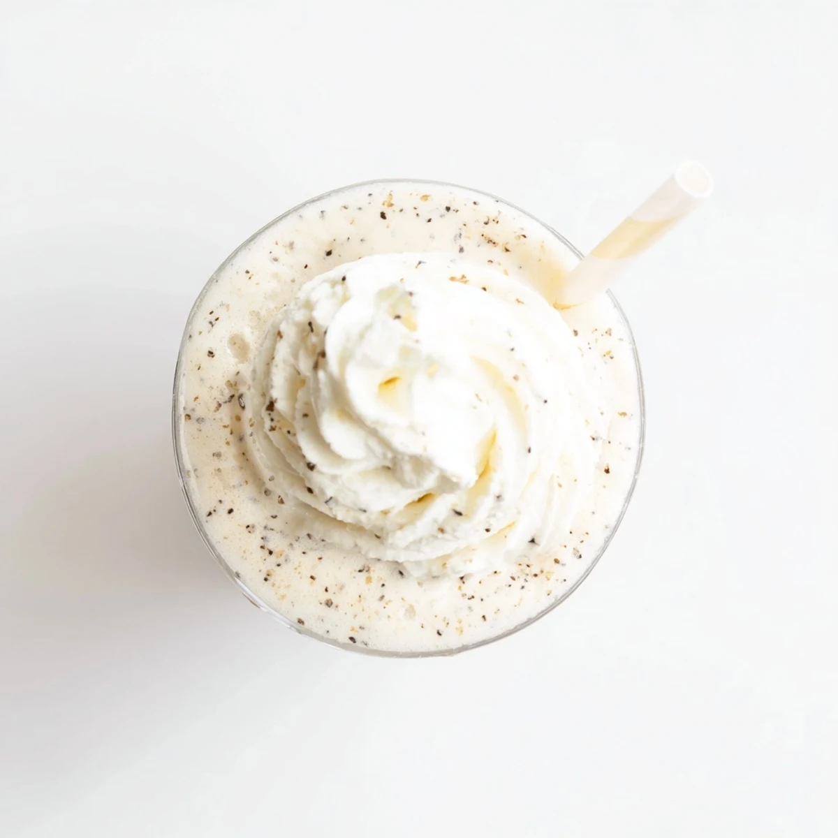 A tall glass of Vanilla Bean Frappuccino topped with whipped cream and a vanilla bean pod beside it.  