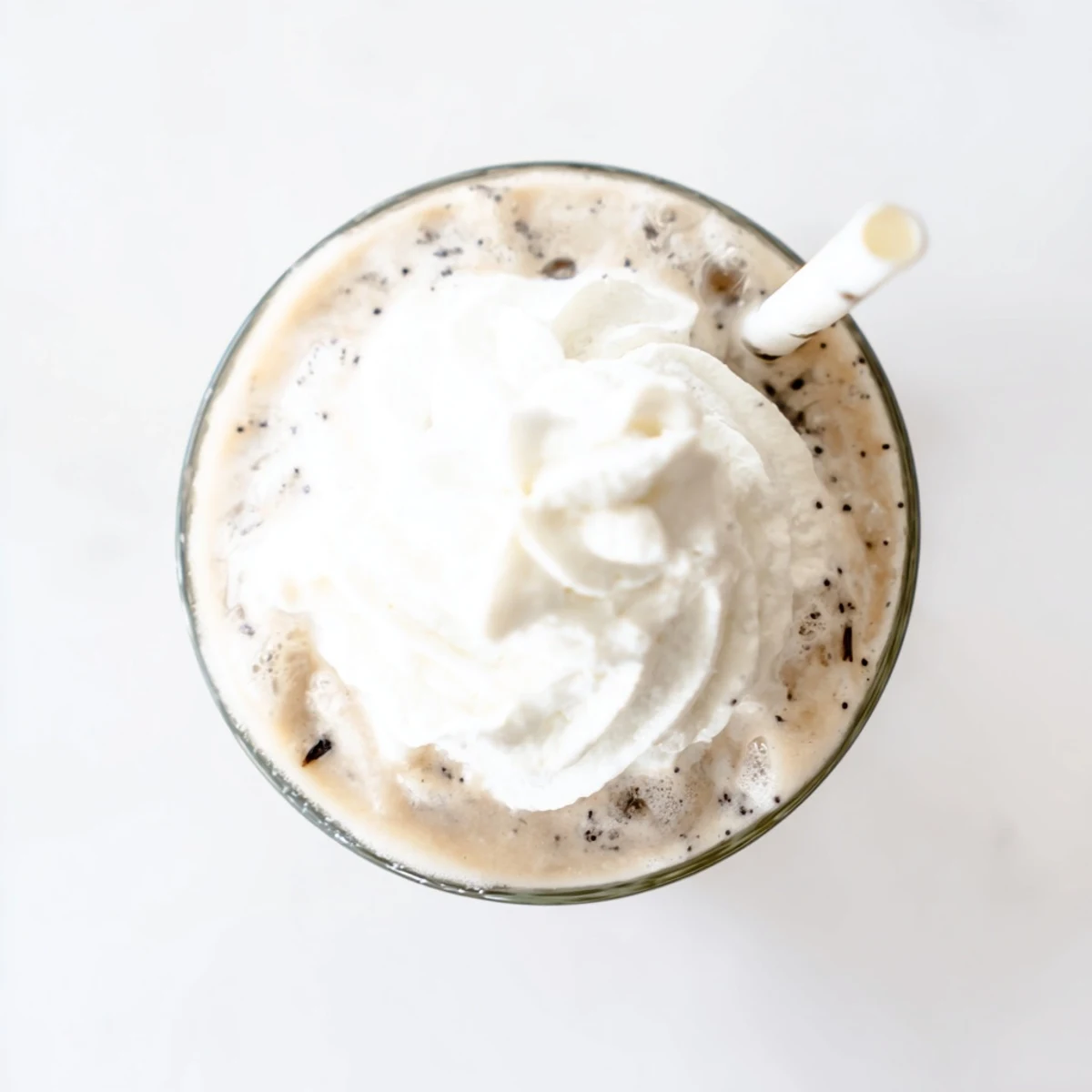 Homemade Vanilla Bean Frappuccino with a straw in a tall glass, blending creamy ice cream and vanilla.