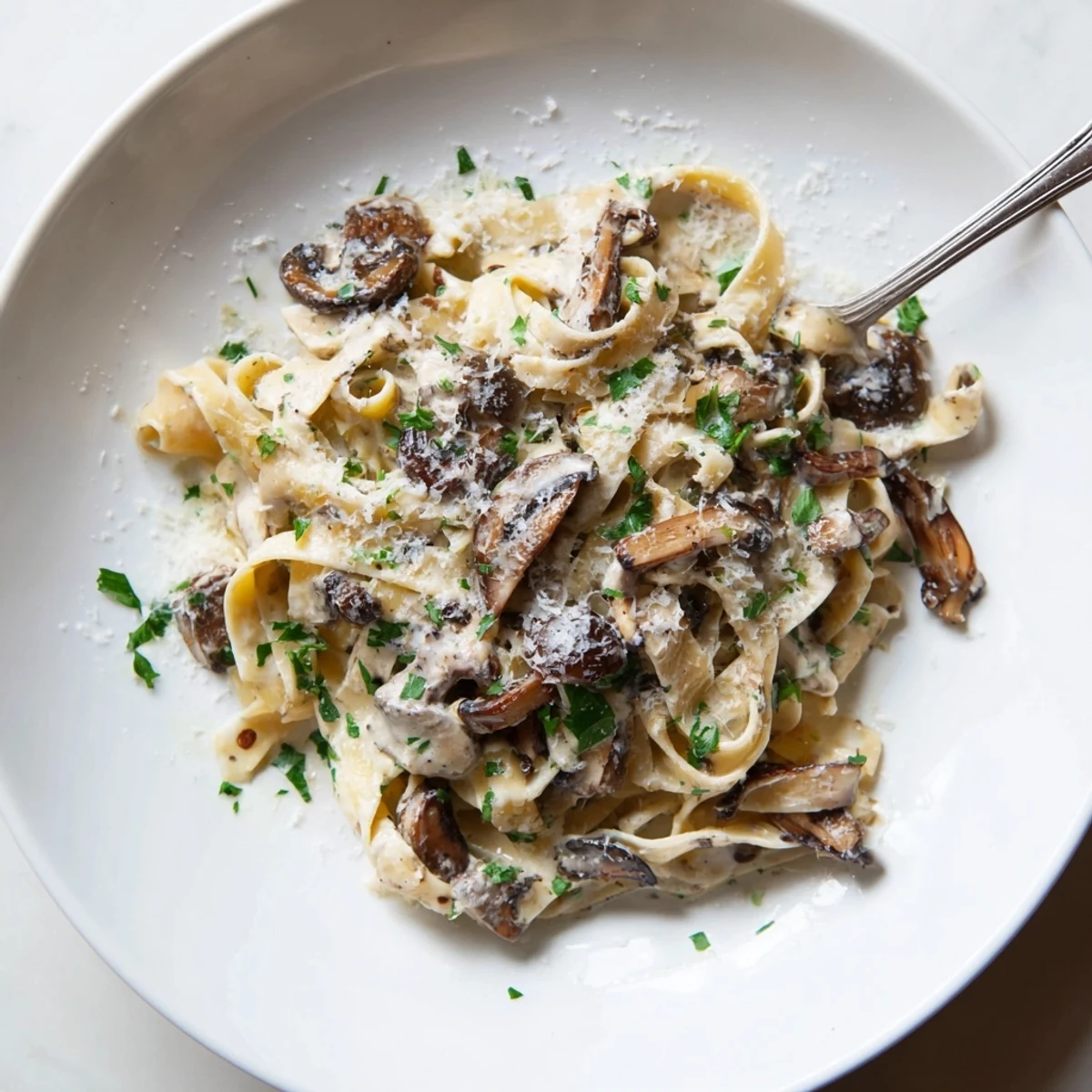 Golden tagliatelle coated in a creamy parmesan sauce with sautéed mushrooms and a drizzle of truffle oil, served on a white plate with fresh parsley garnish.