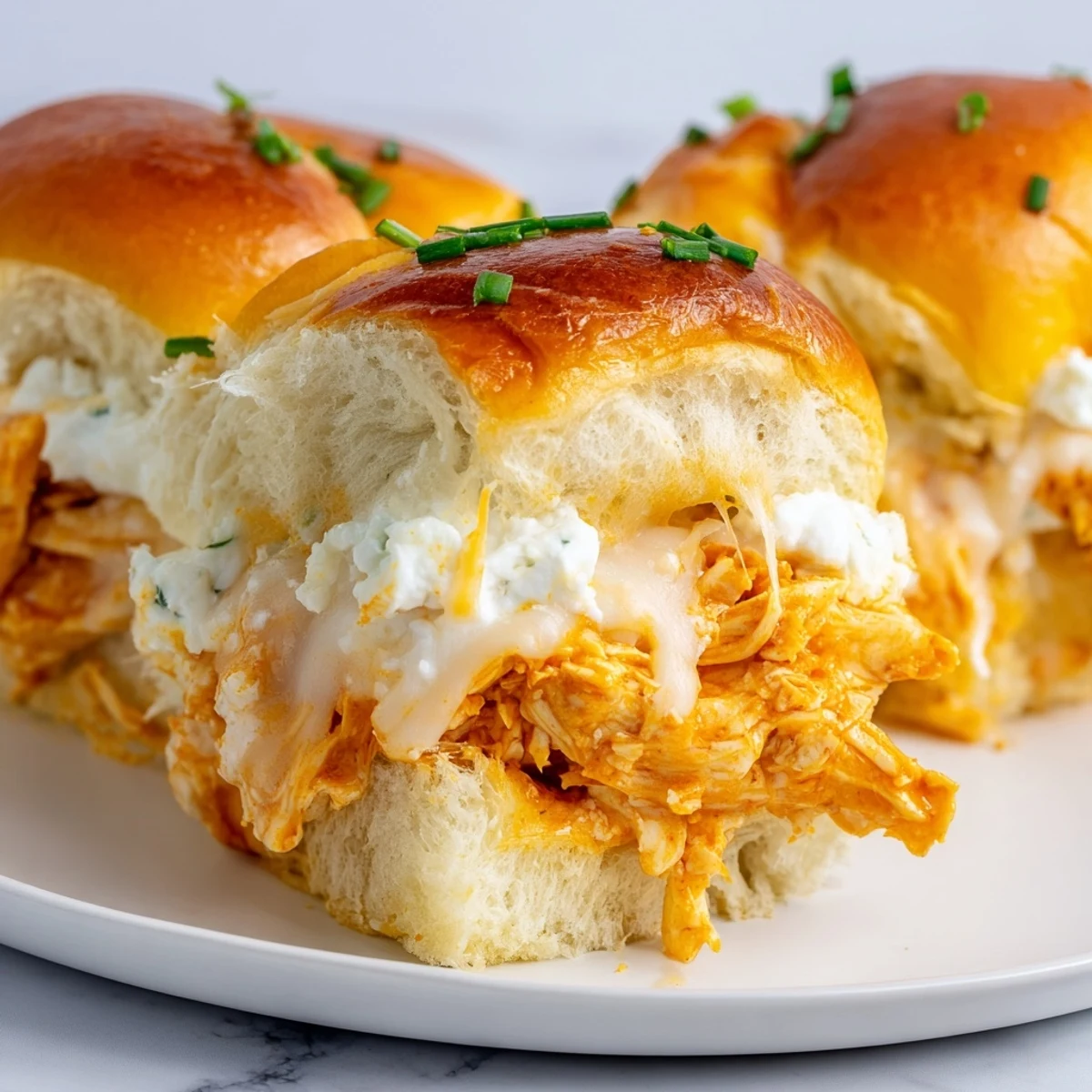 Golden-brown Buffalo Chicken Pizza Dip Sliders fresh from the oven, topped with melted mozzarella and cheddar cheese.