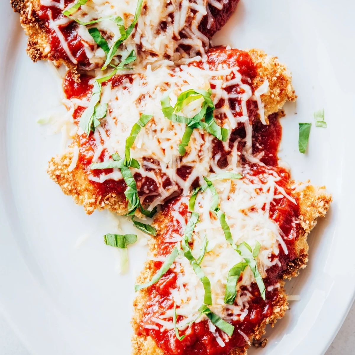 A skillet of sizzling Amazing 15 Minute Keto Chicken Parmesan, garnished with fresh basil and Parmesan, ready to serve with a side of zucchini noodles.