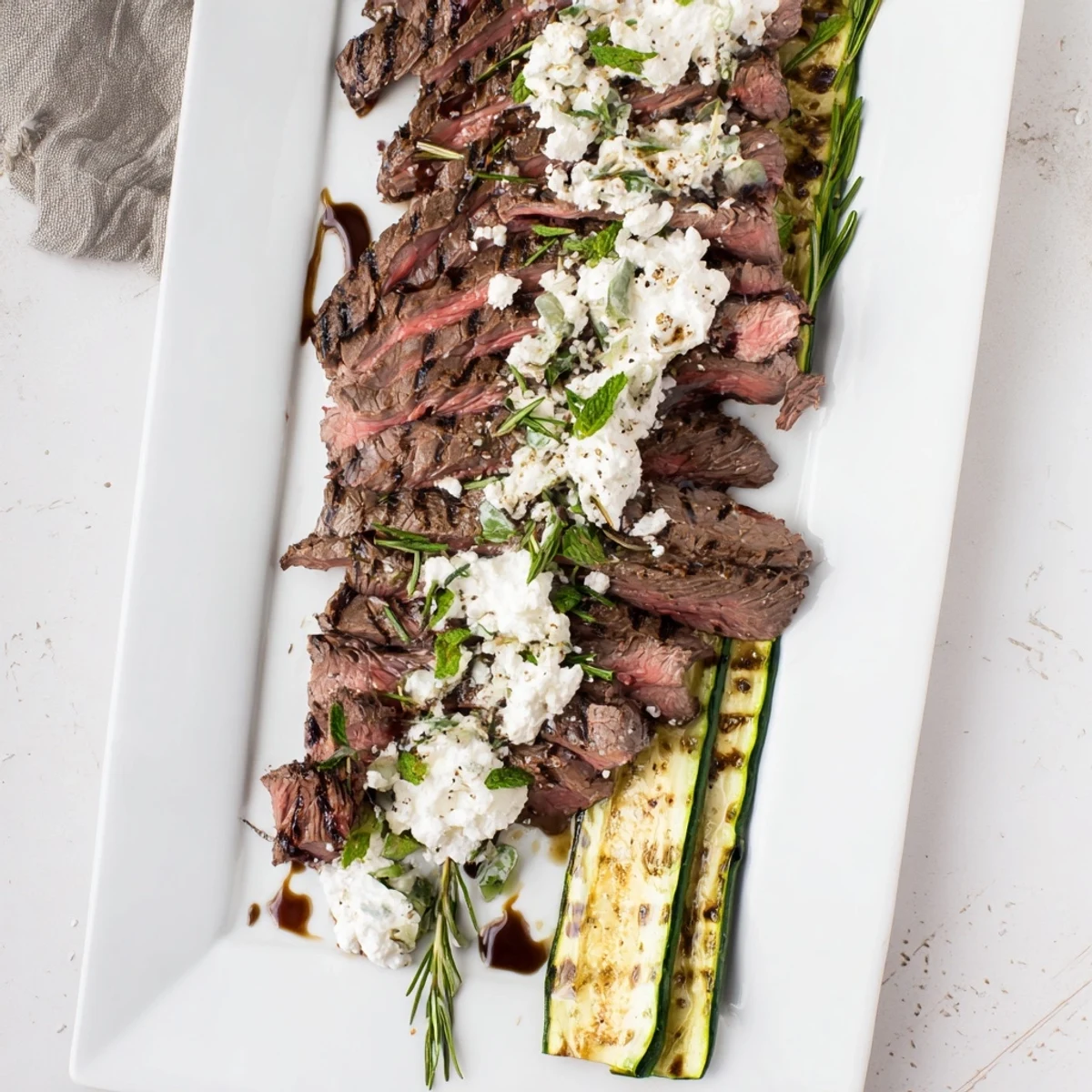 Sliced tender balsamic flank steak served over creamy whipped feta with charred zucchini on a platter.