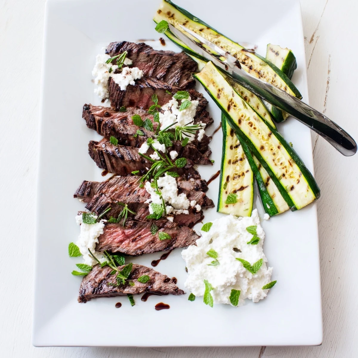 Summer dinner platter featuring balsamic flank steak, grilled zucchini ribbons, and smooth whipped feta spread.