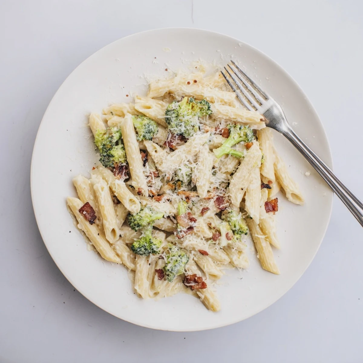 Steaming Bacon Broccoli and Parmesan Pasta served on a dinner plate, garnished with extra Parmesan and a sprinkle of red pepper flakes.