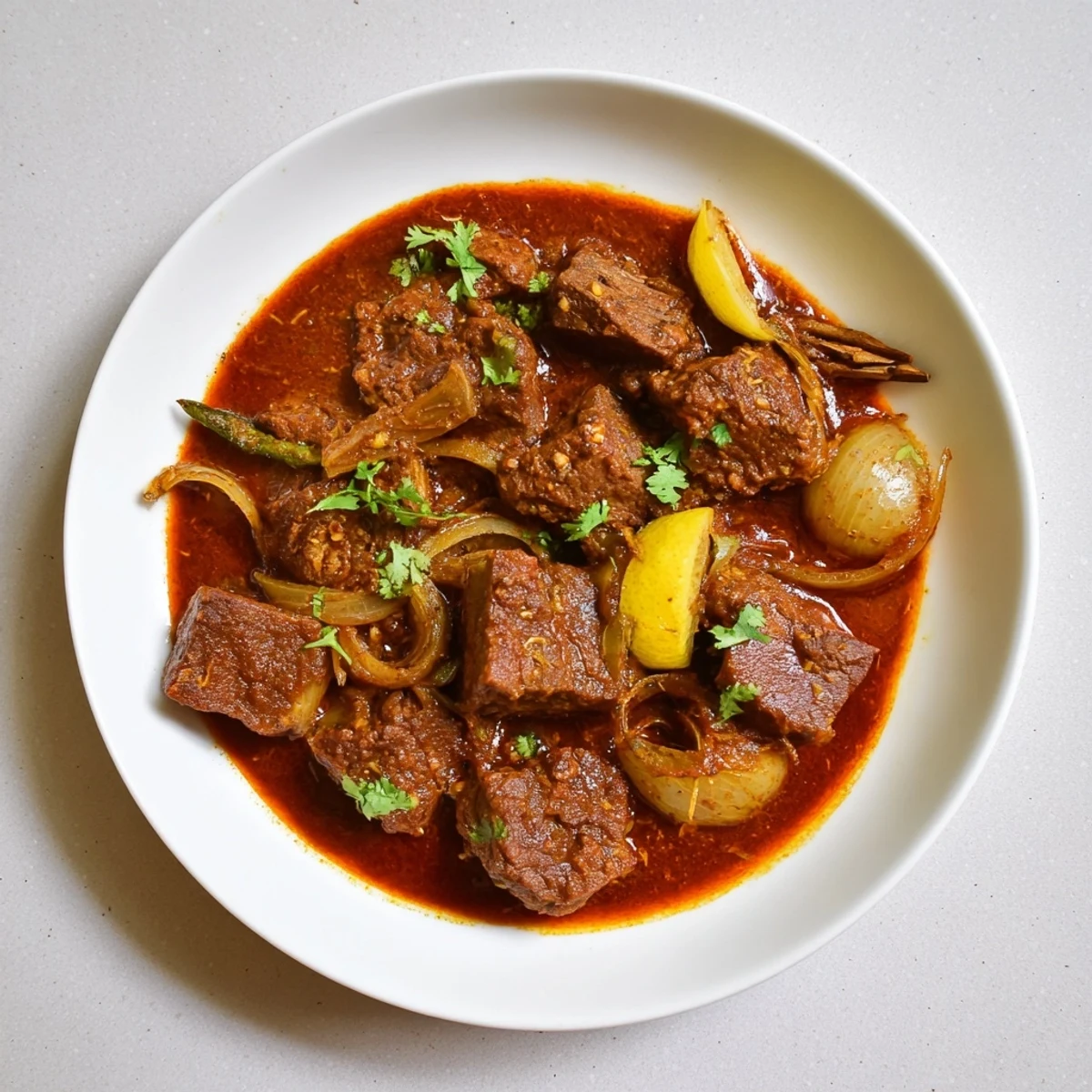 Golden Indian beef curry with tomato gravy served in a white bowl over fluffy basmati rice