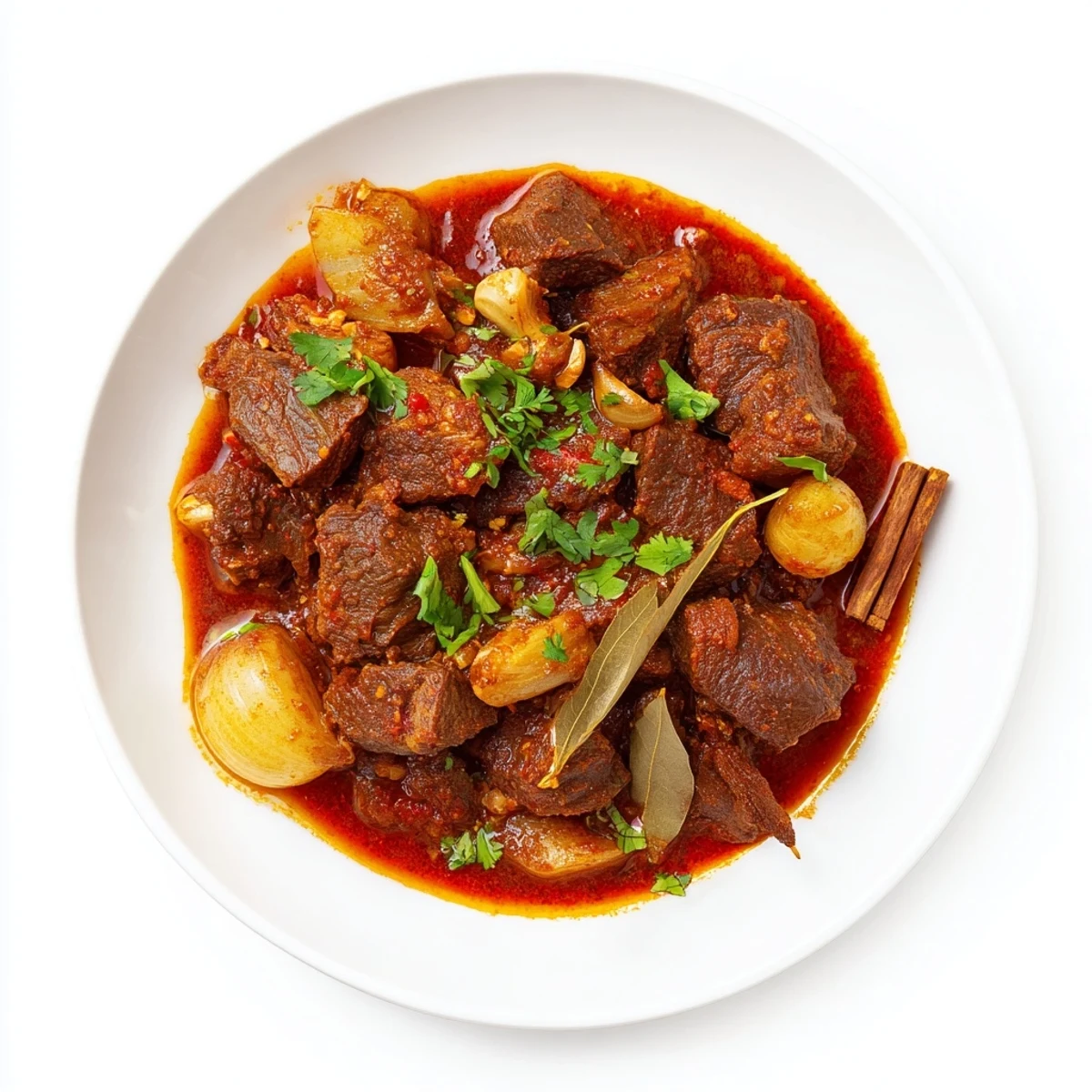 Steaming bowl of aromatic beef curry with thick red gravy topped with chopped cilantro and lemon wedge