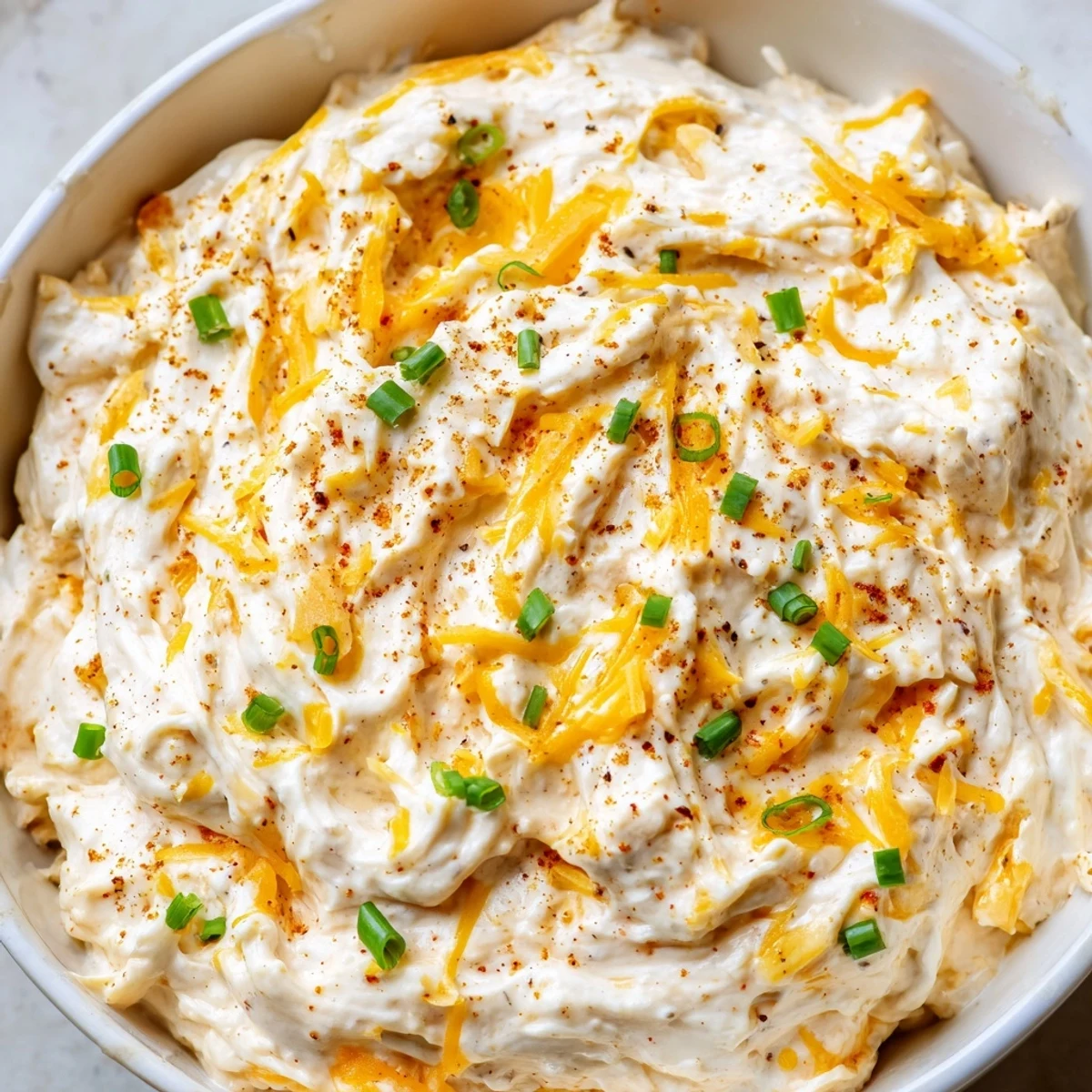Rich cheddar and garlic savory pretzel dip in a white bowl garnished with green onions
