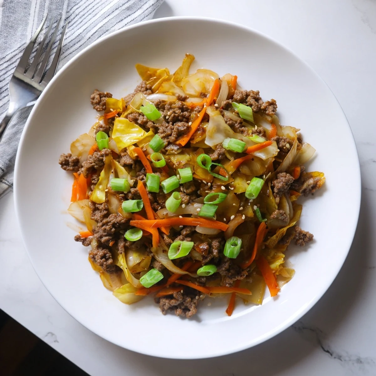 Sizzling skillet of Asian-inspired ground beef and cabbage stir fry topped with fresh green onion garnish