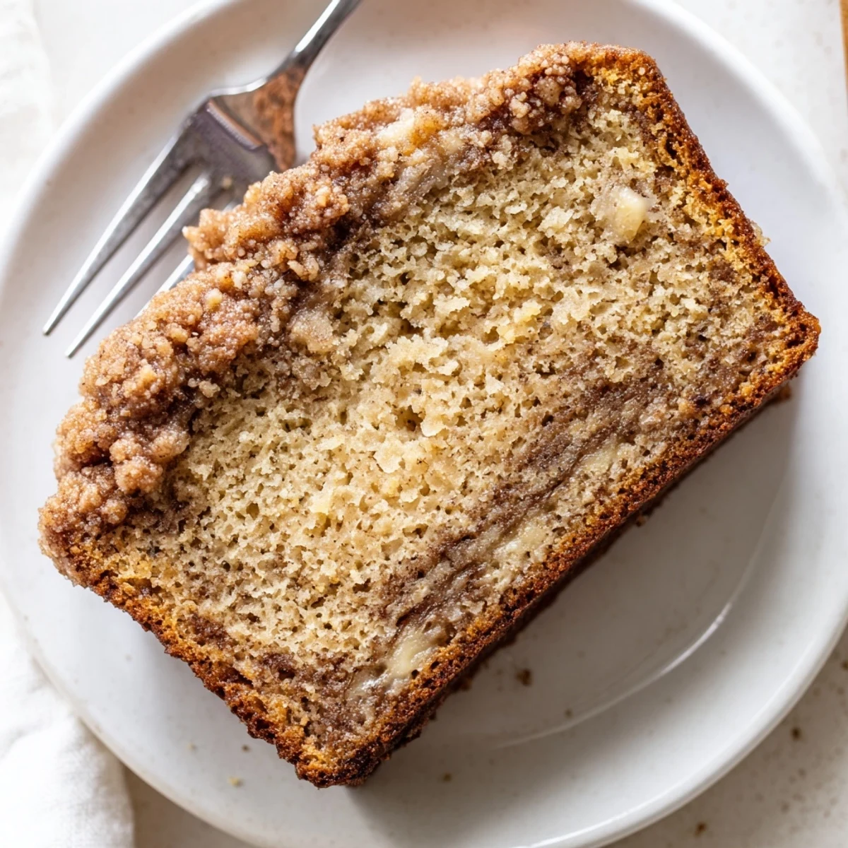 Freshly sliced banana bread with moist texture and cinnamon crumb topping on white plate