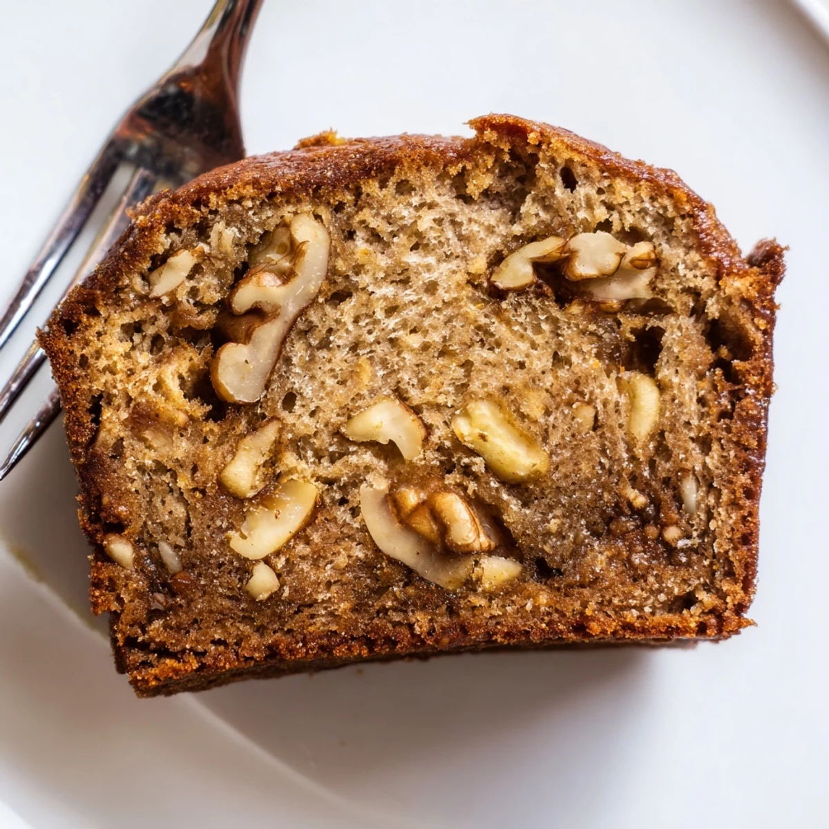 Golden brown ultimate banana nut bread loaf topped with toasted walnuts on a wooden cutting board