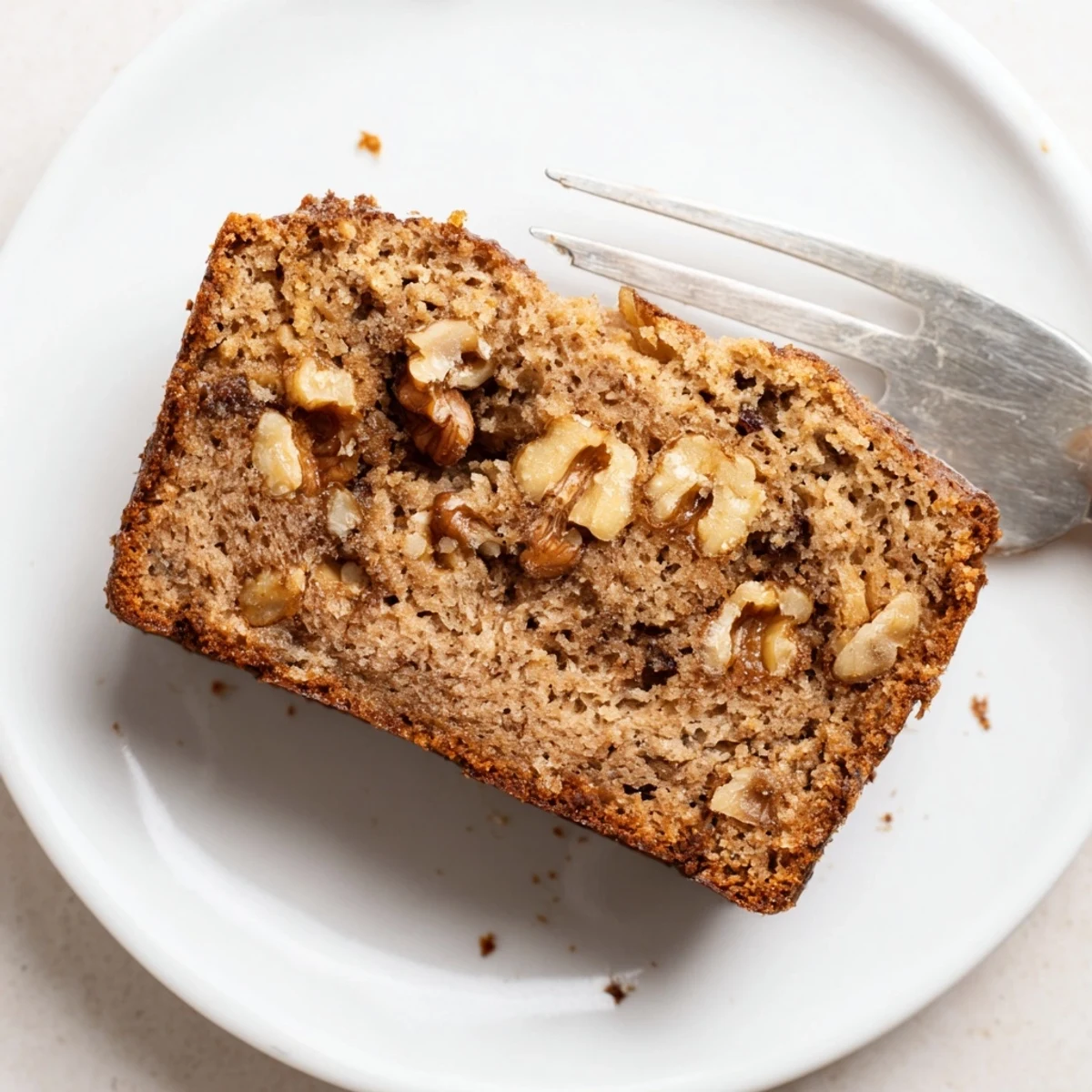 Thick slice of moist ultimate banana nut bread revealing a tender crumb dotted with chopped walnuts