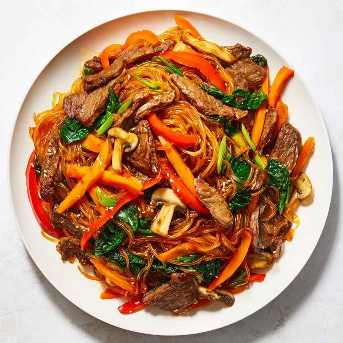 Steaming bowl of Korean beef noodles with tender beef slices and colorful vegetables in glossy sauce