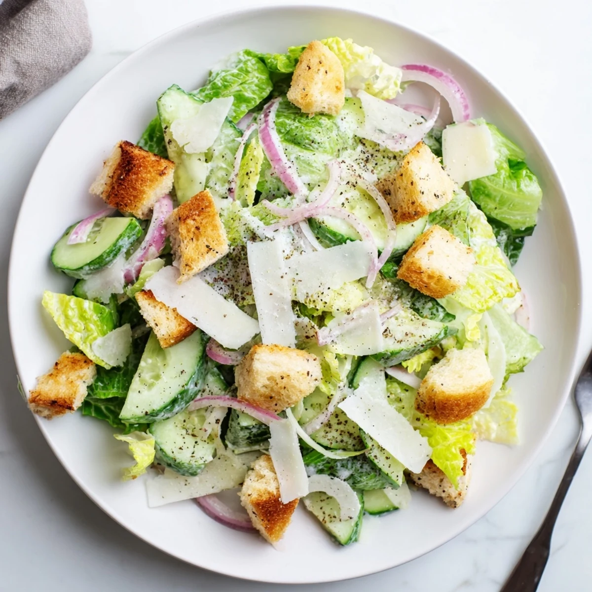 Colorful bowl of cucumber Caesar salad featuring crunchy croutons, shaved Parmesan, and tangy dressing coating crisp lettuce and cucumber slices