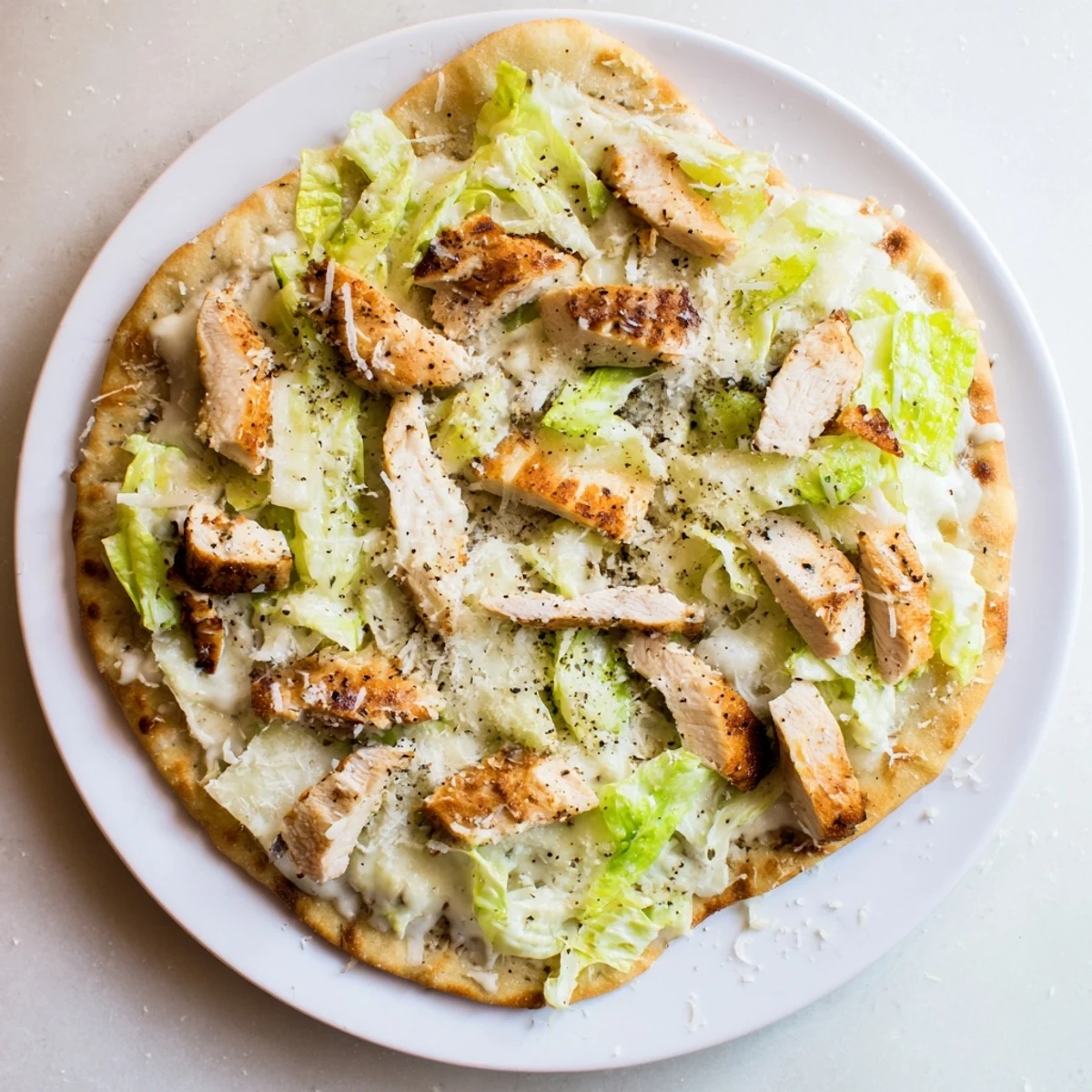 Grilled chicken Caesar flatbread topped with creamy dressing and shaved parmesan cheese
