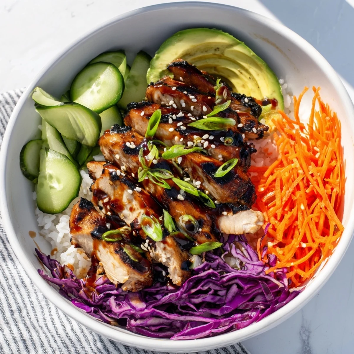 Vibrant bowl featuring sweet and savory Korean BBQ chicken thighs atop fluffy rice with crisp carrots cucumber and avocado garnish