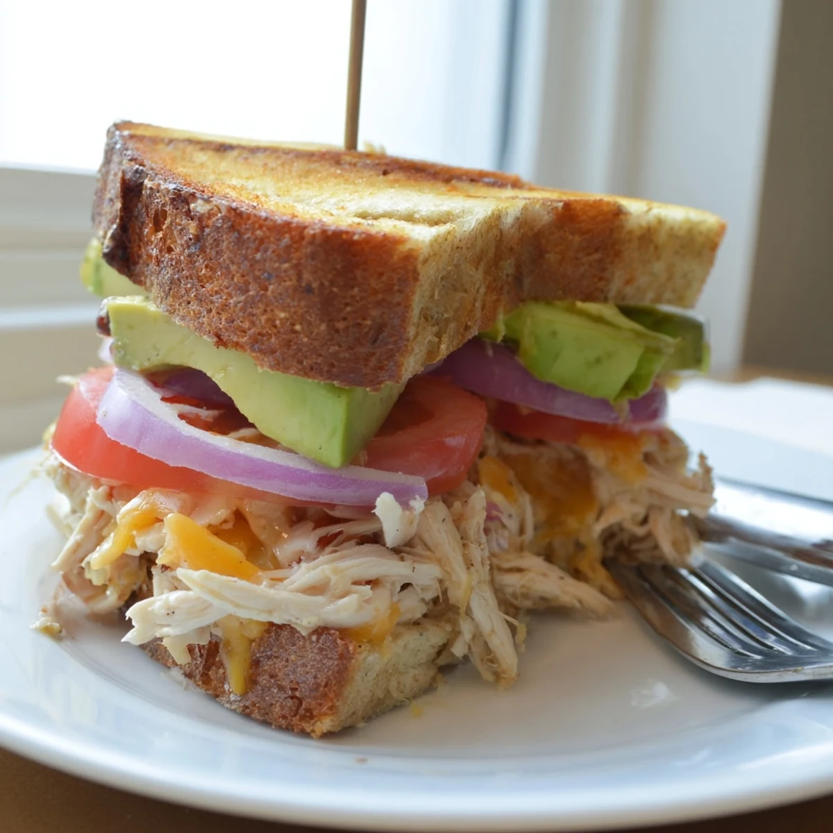 Warm Chicken Avocado Melt Sandwich on a white plate, fresh green side salad visible nearby