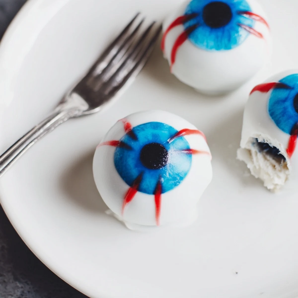 Glossy white Halloween Cake Eyeballs with blue irises on a dark tray