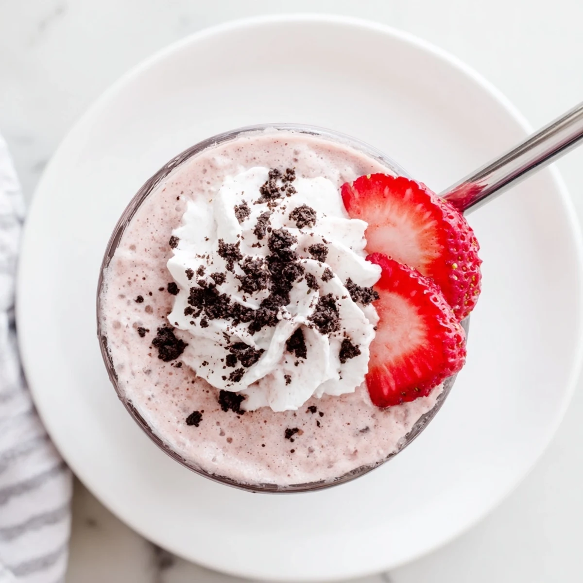 Two tall glasses of blended strawberry Oreo milkshake garnished with fluffy whipped cream