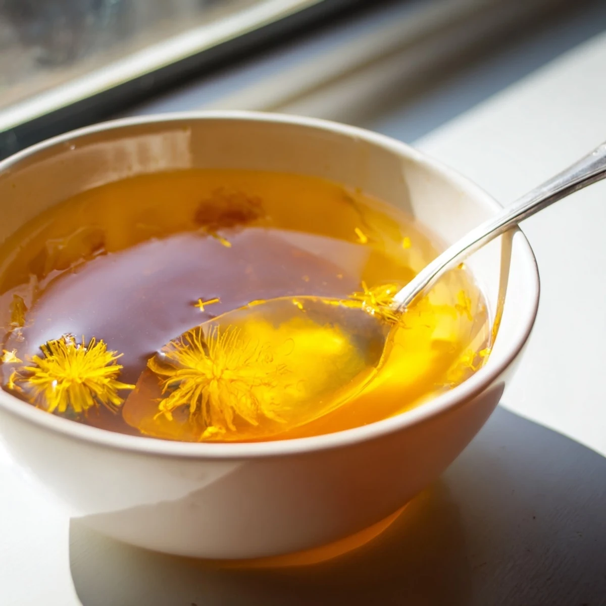 A jar of homemade fresh dandelion jelly drizzled over a scone with cheese