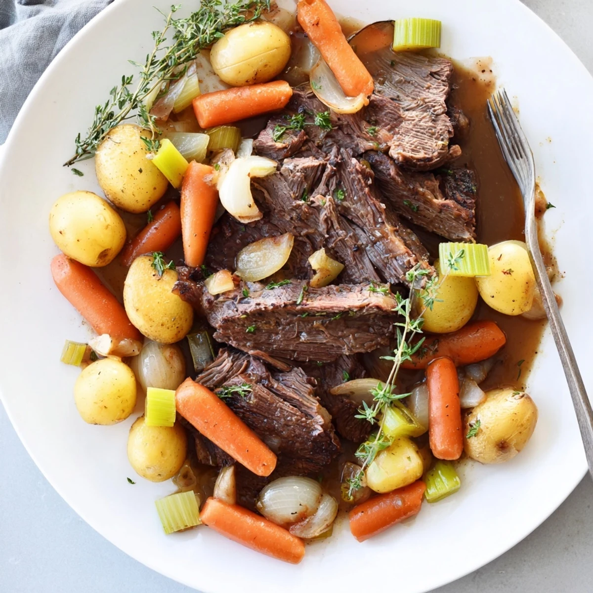Golden seared herb braised beef chuck roast surrounded by carrots, celery, and onions