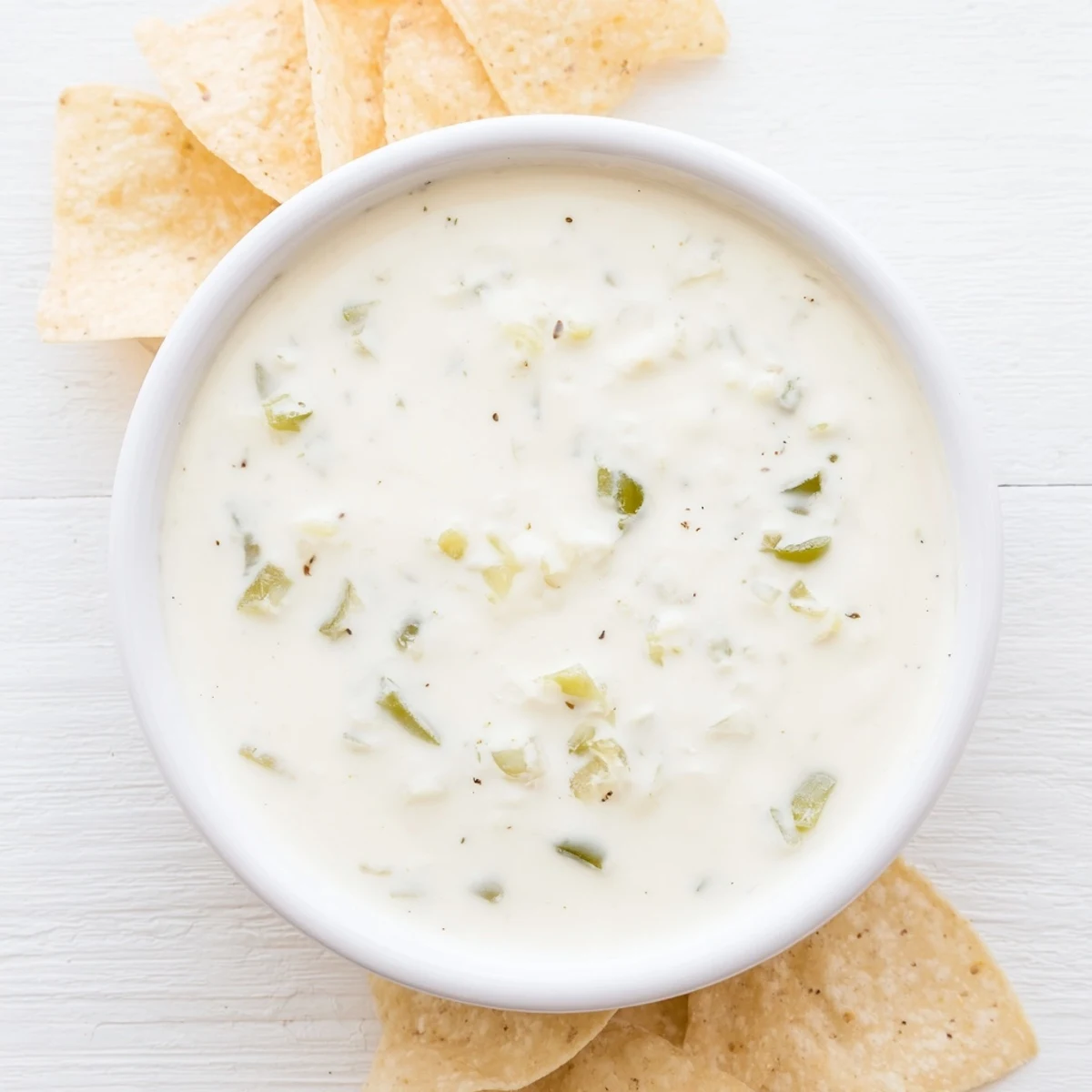 Golden white queso dip bubbling in a skillet topped with fresh diced jalapeños