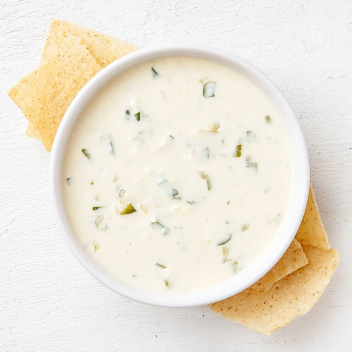 Smooth white queso dip with melted cheese drizzled over crunchy tortilla chip scoops