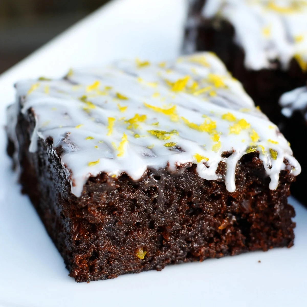 Golden lemon zest brownies drizzled with white glaze and fresh citrus garnish on a white plate