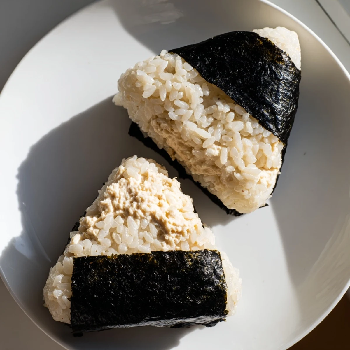 Handheld Japanese tuna mayonnaise rice ball with savory creamy fish filling center