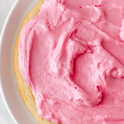 Plate a Crumbl Pink Sugar Cookie next to a glass of cold milk, with pink frosting swirled on top.