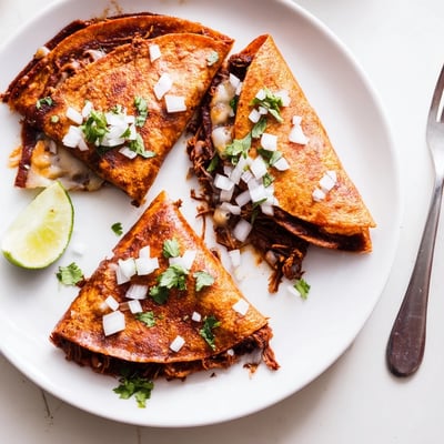 Slow cooker birria tacos garnished with fresh cilantro, onion, and lime wedges