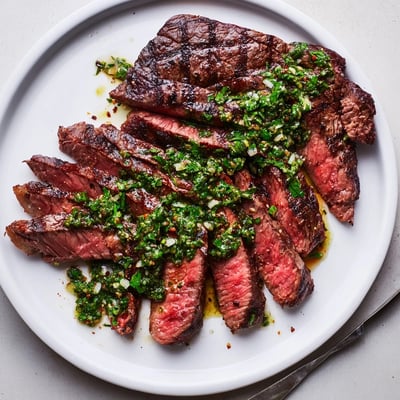 Sliced medium-rare steak resting, bright green sauce spooned over — Chimichurri Steak Recipe